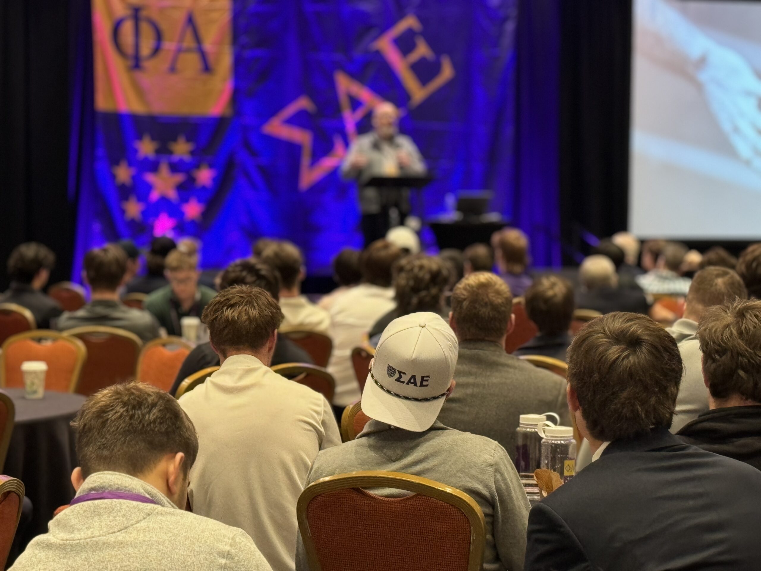 SAE brothers listening to a public speaker at event